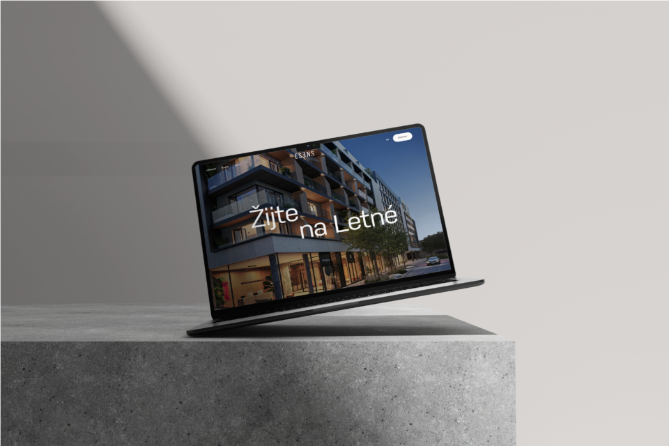 A laptop on a concrete surface displays a webpage with the text “Live in Letná” and an image of a modern building. Modern living in an attractive Prague neighborhood.