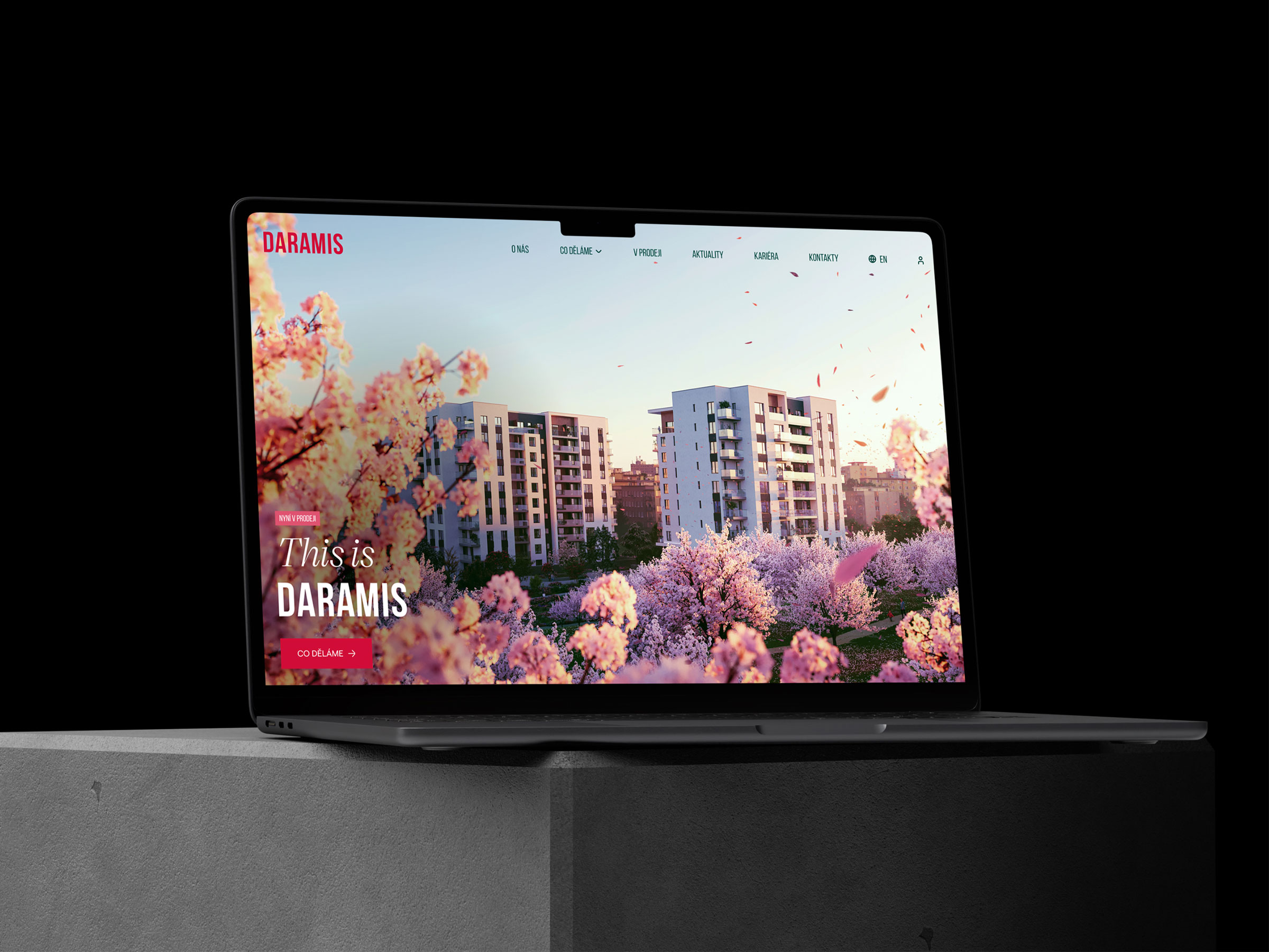 Notebook zobrazuje webovou stránku společnosti Daramis, zaměřenou na moderní architekturu s květinovou tématikou na pozadí, umístěný na betonové ploše.