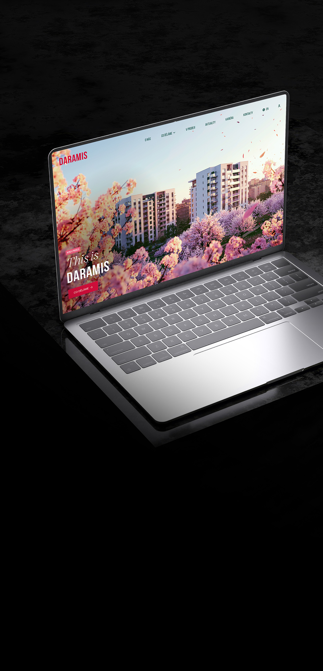 Notebook zobrazuje webovou stránku s obrázkem moderních bytových domů a rozkvetlých stromů na obrazovce. Webová stránka náleží společnosti Daramis.