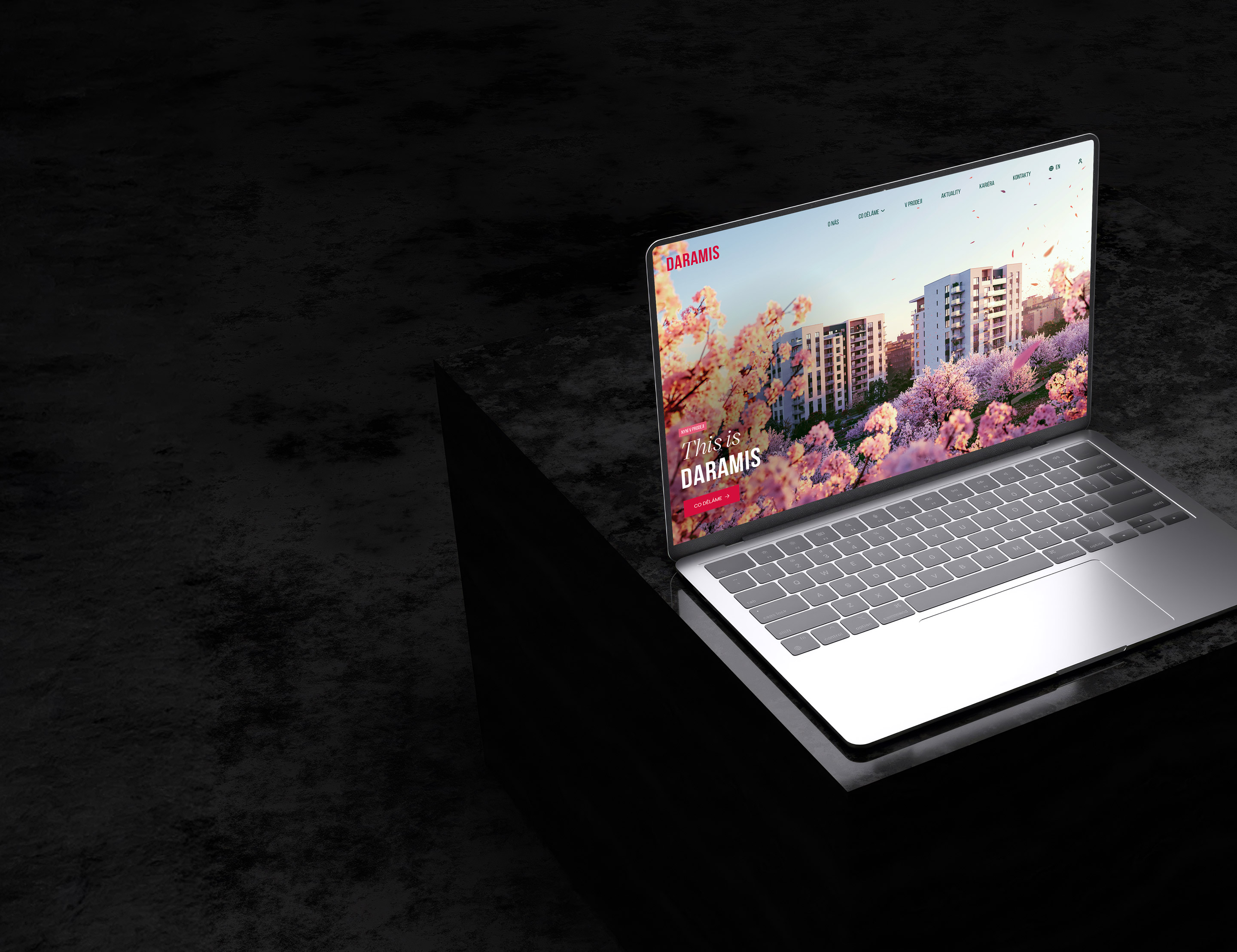 Otevřený notebook s moderním designem na tmavém pozadí s obrazovkou zobrazující online webovou stránku městského projektu s budovami a stromy v pastelových barvách.
