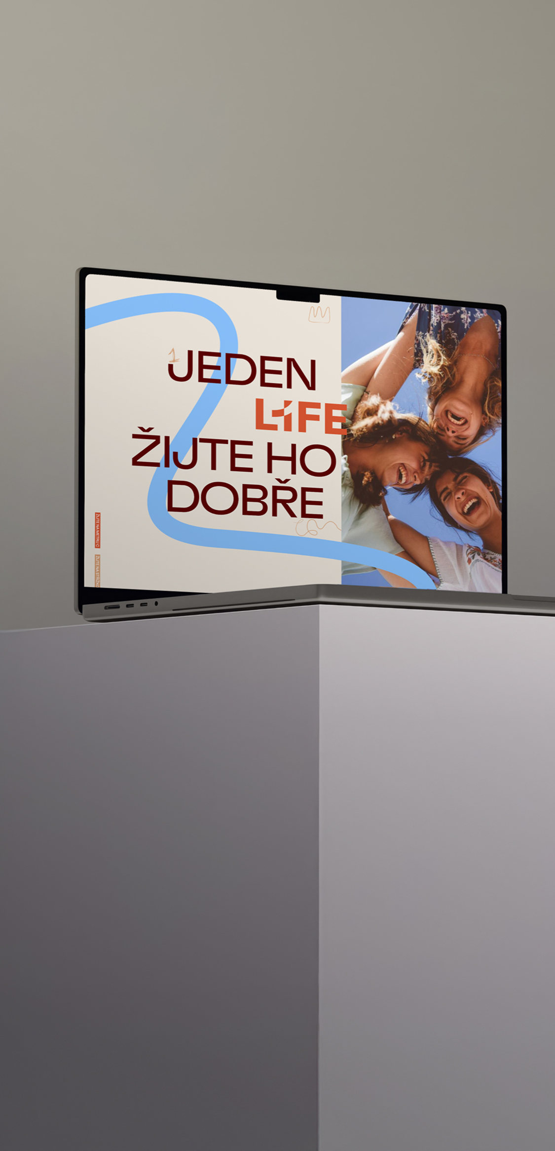 A laptop with an image of three smiling people on the screen, along with the text “One life—live it well”; its modern design and gray background highlight the device’s style and functionality