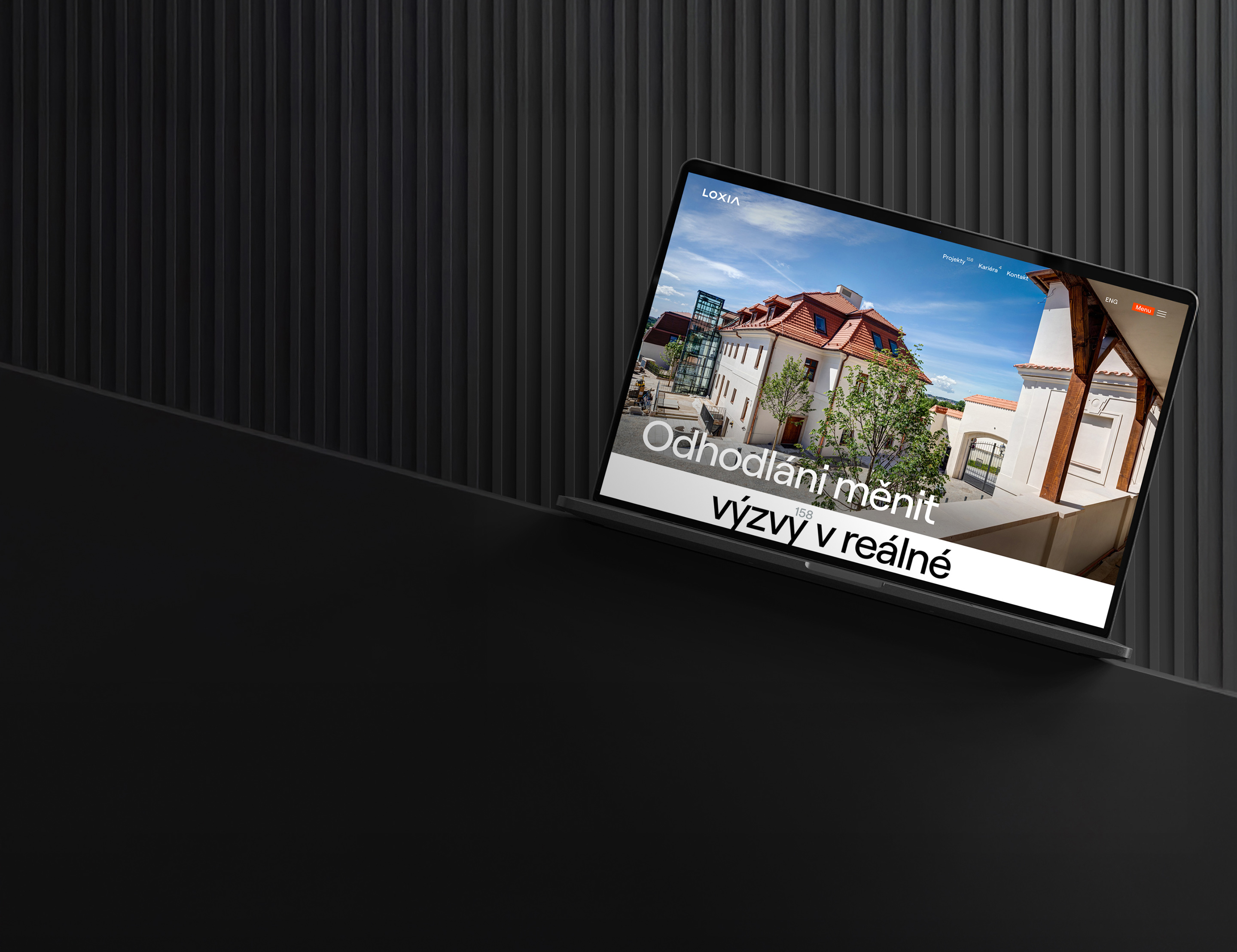 Notebook zobrazující webovou stránku architektonického projektu s moderní budovou na stříbrném pozadí s textem Odhodlaní měnit výzvy v reálné