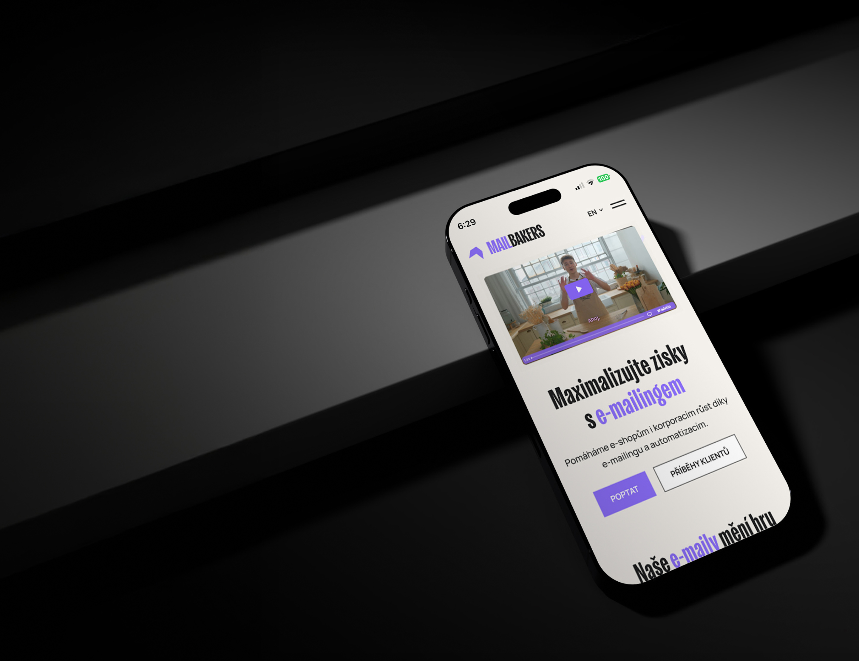 Mobilní telefon zobrazuje e-commerce webovou stránku s textem o maximalizaci prodeje s e-mailingem. Leží na tmavém povrchu s moderním a elegantním vzhledem.
