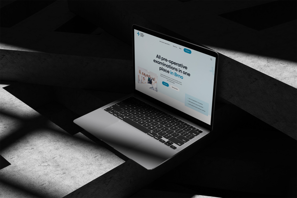 A laptop open on a concrete surface displays a minimalist web design with text on the screen. The slanted light and shadows create a dramatic visual effect.