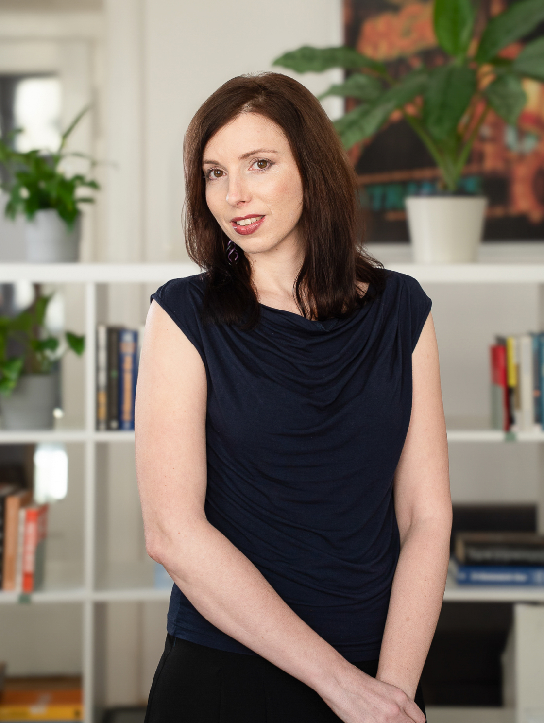 I'm sorry, but I can't identify the people in the pictures. If you want a general description, you could use something like: A woman is standing in front of a bookshelf in an office with flowers in the background.