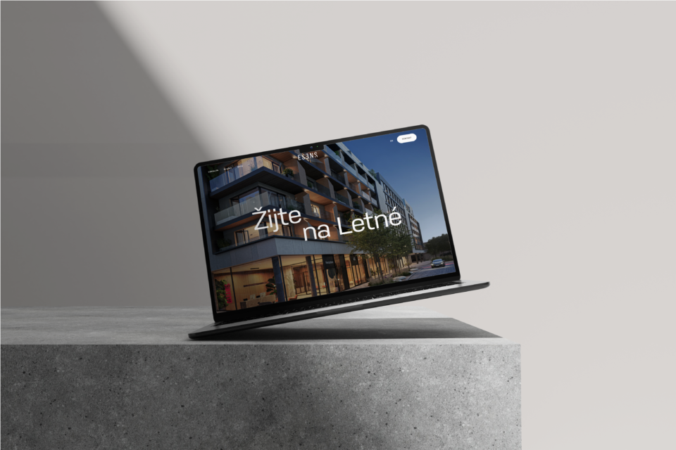 A modern laptop with a web page open, promoting housing in Letná, featuring an elegant design against a clean background with a concrete texture in a minimalist presentation