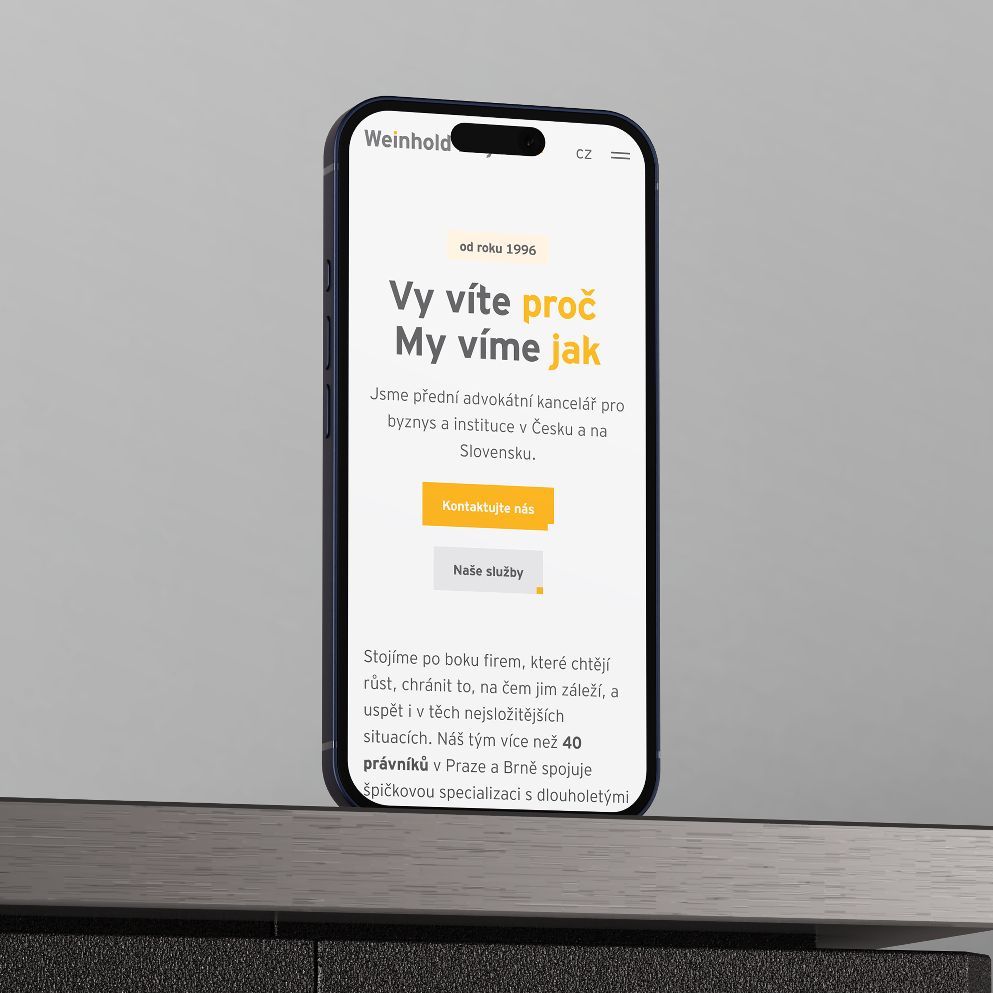 A smartphone displays a law firm's website, which offers services to businesses and institutions in the Czech Republic and Slovakia, in a modern design on a wooden table.